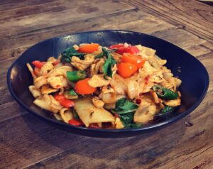 Chicken drunken noodles with tomatoes, peppers and Thai basil in a black bowl. (Photo: Sisters Thai/Facebook)