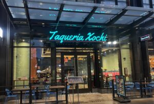 Exterior of Taqueria Xochi with patio and sign in turquoise neon. (Photo: Taqueria Xochi)