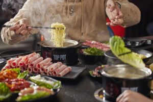 A woman cooking noodles in a hot pot at her table surrounded by plates of meats and vegetables. (Photo: Top Pot)