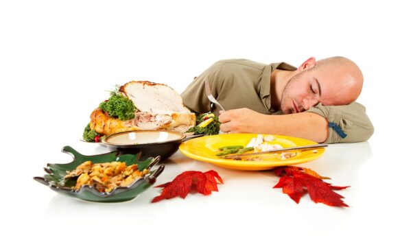 Man falling asleep aat table holding silverware after dinner surrounded by leftover turkey and other food. (Photo: Sean Locke/Getty Images)