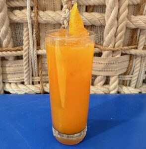 All Set's The Concept of an Orange Drink in a tall glass with an orange peel on top sitting on a table with a blue tablecloth and thick rope in the background. (Photo: All Set)