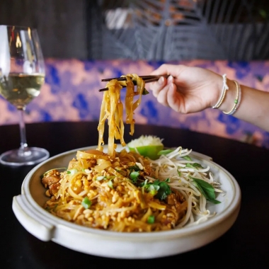 A woman's hand holding chopsticks picks up noodles from a plate of pad Thai. (Photo: Andrew Noh)
