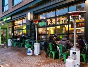Exterior of El Sapo Cuban Social Club with people eating outside at round tables in front of glass garage doors. (Photo: El Sapo Cuban Social Club/Facebook)