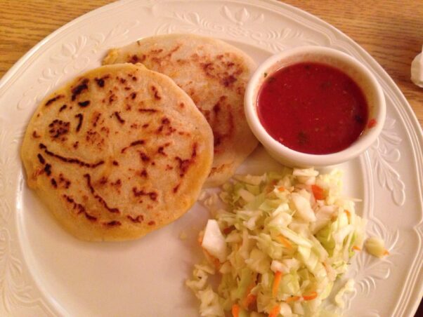 Two pupusas on a white plate with cabbage slaw and tomato salsa. (Photo: David R./Yelp)