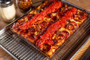 A pepperoni Detriot-style pizza covered with sauce on top sitting on a wire rack. (Photo: Little Beast Cafe & Bistro)